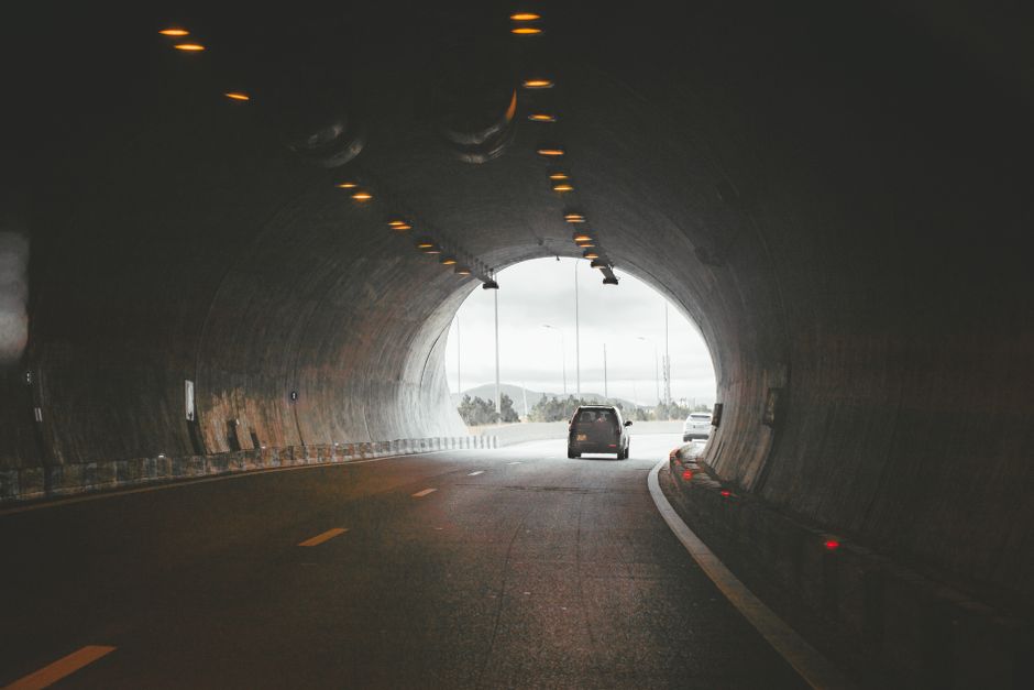 A view from inside a graffiti-covered underpass tunnel, with dark, weathered concrete walls and ceiling adorned with vibrant street art, including a large cartoonish bird and various tags. The tunnel